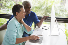 Senior African-American couple sitting at a table viewing a computer screen.